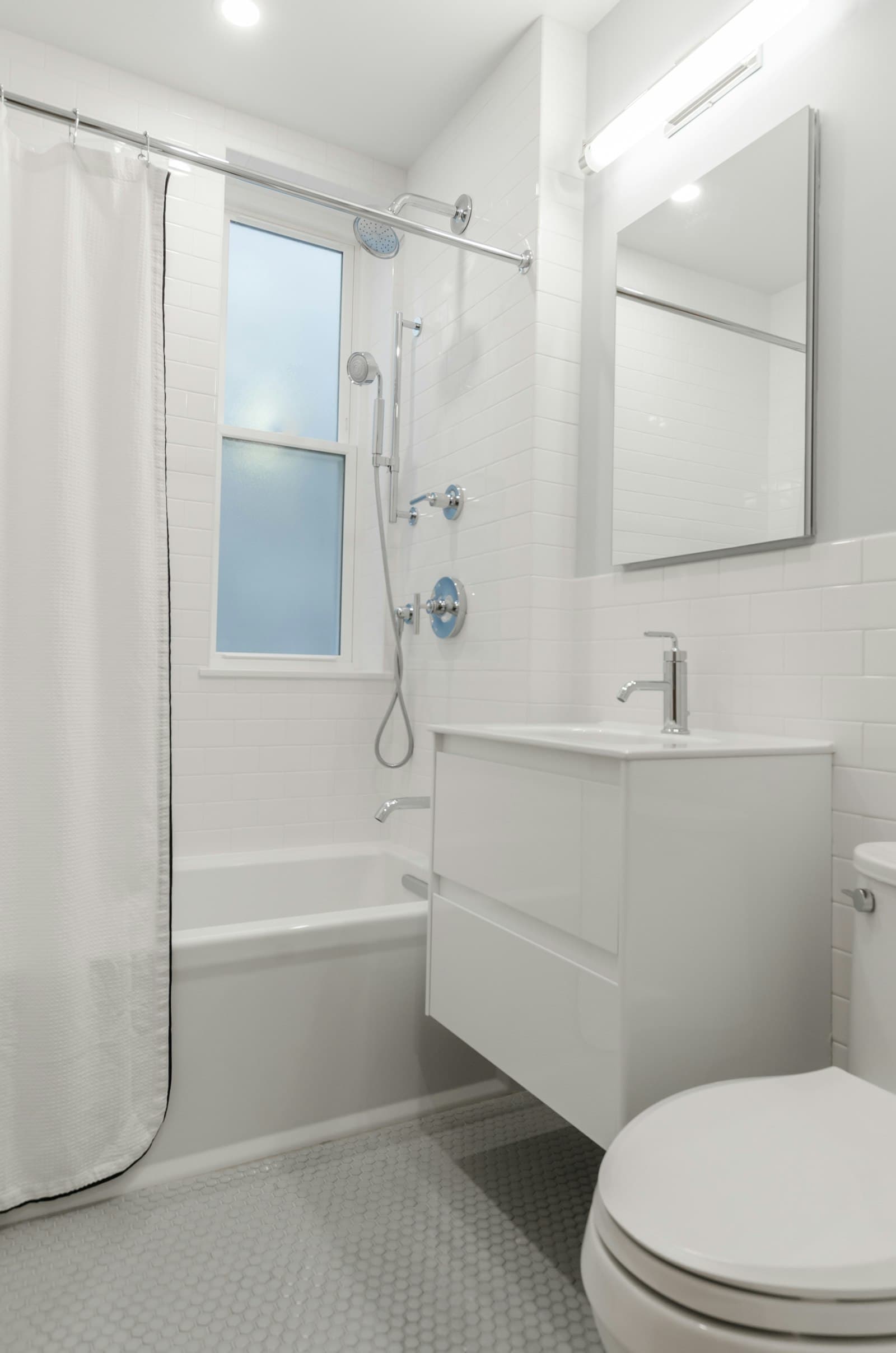 Bagno compatto d'appartamento con vasca, doccia a soffione e rivestimento bianco a mosaico.