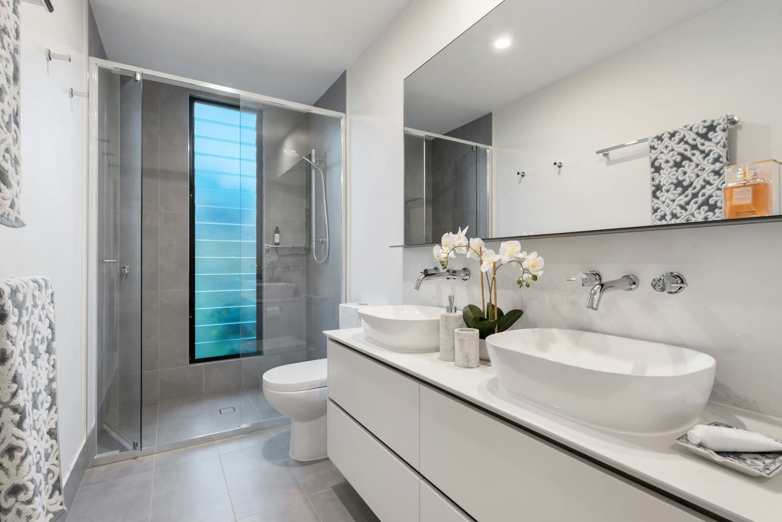 Bagno con doppio lavabo d'appoggio, box doccia in cristallo e rivestimenti grigi.