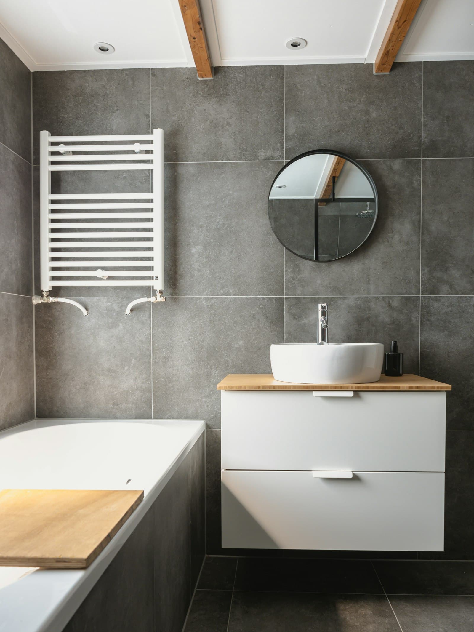 Bagno ristrutturato con scaldasalviette bianco, mobile sospeso e pareti in gres effetto cemento.